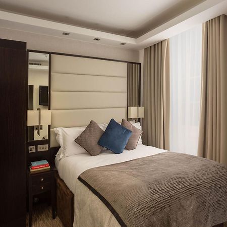 Montcalm Brewery Townhouse Londres Exterior foto The image shows a cozy bedroom. It features a comfortable double bed with a light-colored duvet and decorative pillows in shades of blue and gray. The headboard is upholstered in a soft material, and there are bedside lamps on either side of the bed.