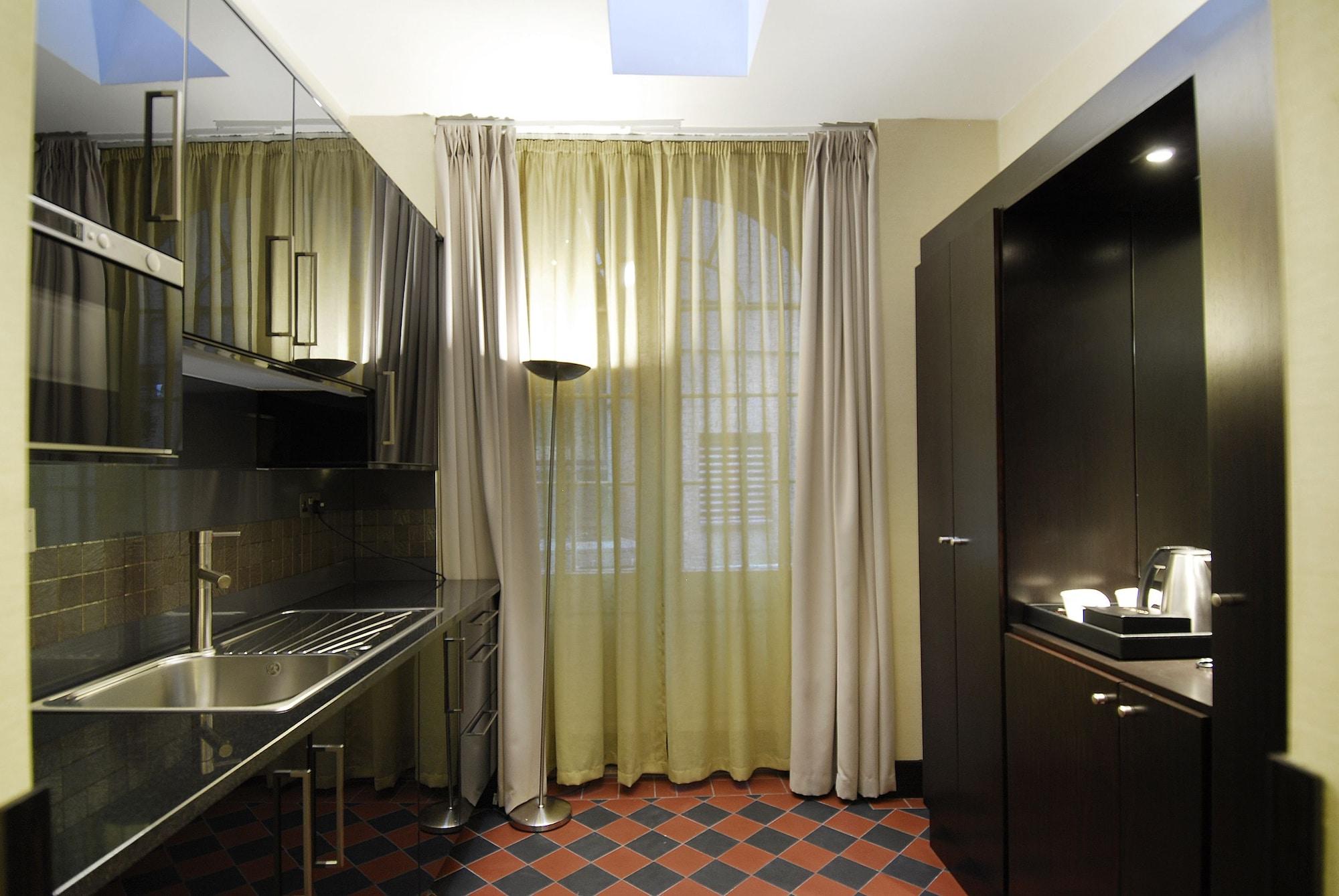 Montcalm Brewery Townhouse Londres Exterior foto The photo shows a modern kitchen space. On the left side, there is a sleek countertop and kitchen cabinets in a dark finish. The backsplash appears shiny, reflecting the surroundings. To the right, there is a tall black cabinet. A window is covered w