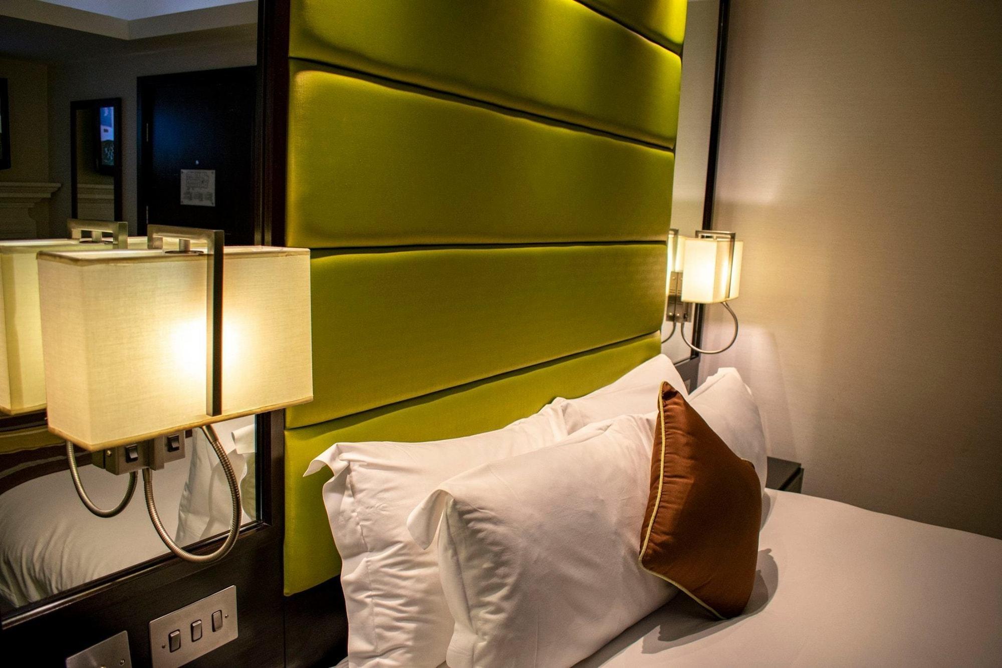 Montcalm Brewery Townhouse Londres Exterior foto The photo shows a modern hotel room with a stylish design. The focal point is a large bed with white pillows and a decorative brown pillow. The headboard is bright green and has a textured appearance. On either side of the bed, there are wall lamps t