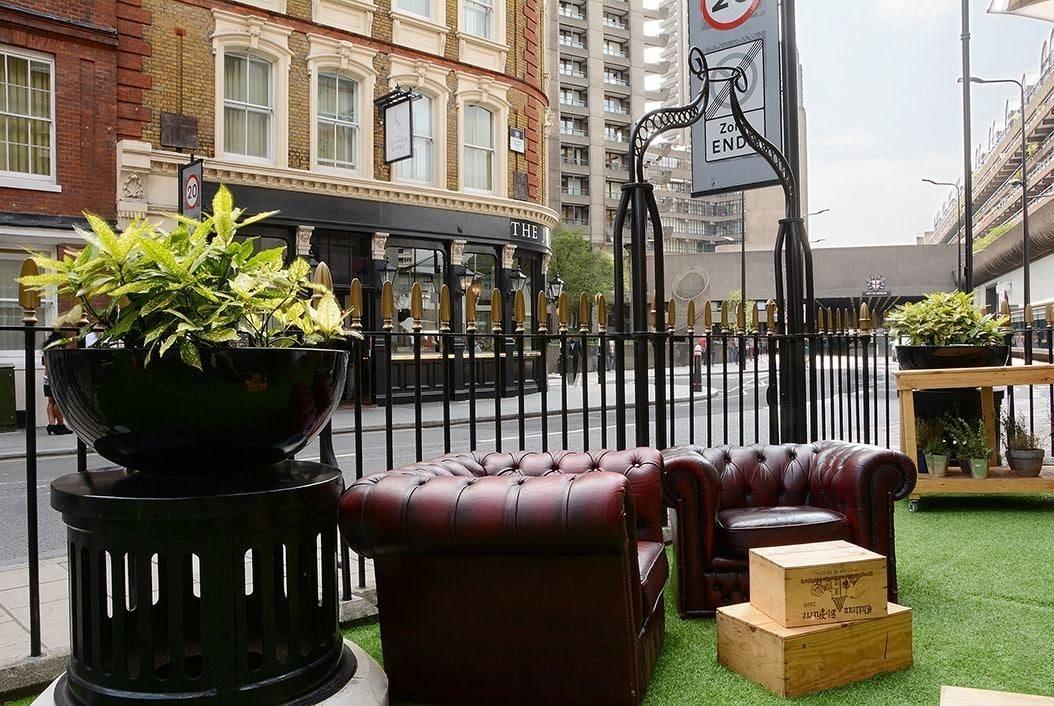 Montcalm Brewery Townhouse Londres Exterior foto The photo shows a street scene with a cozy outdoor seating area. There are two plush, dark leather couches arranged on green grass, creating a welcoming atmosphere. Surrounding the seating are large planters with vibrant plants. In the background, th