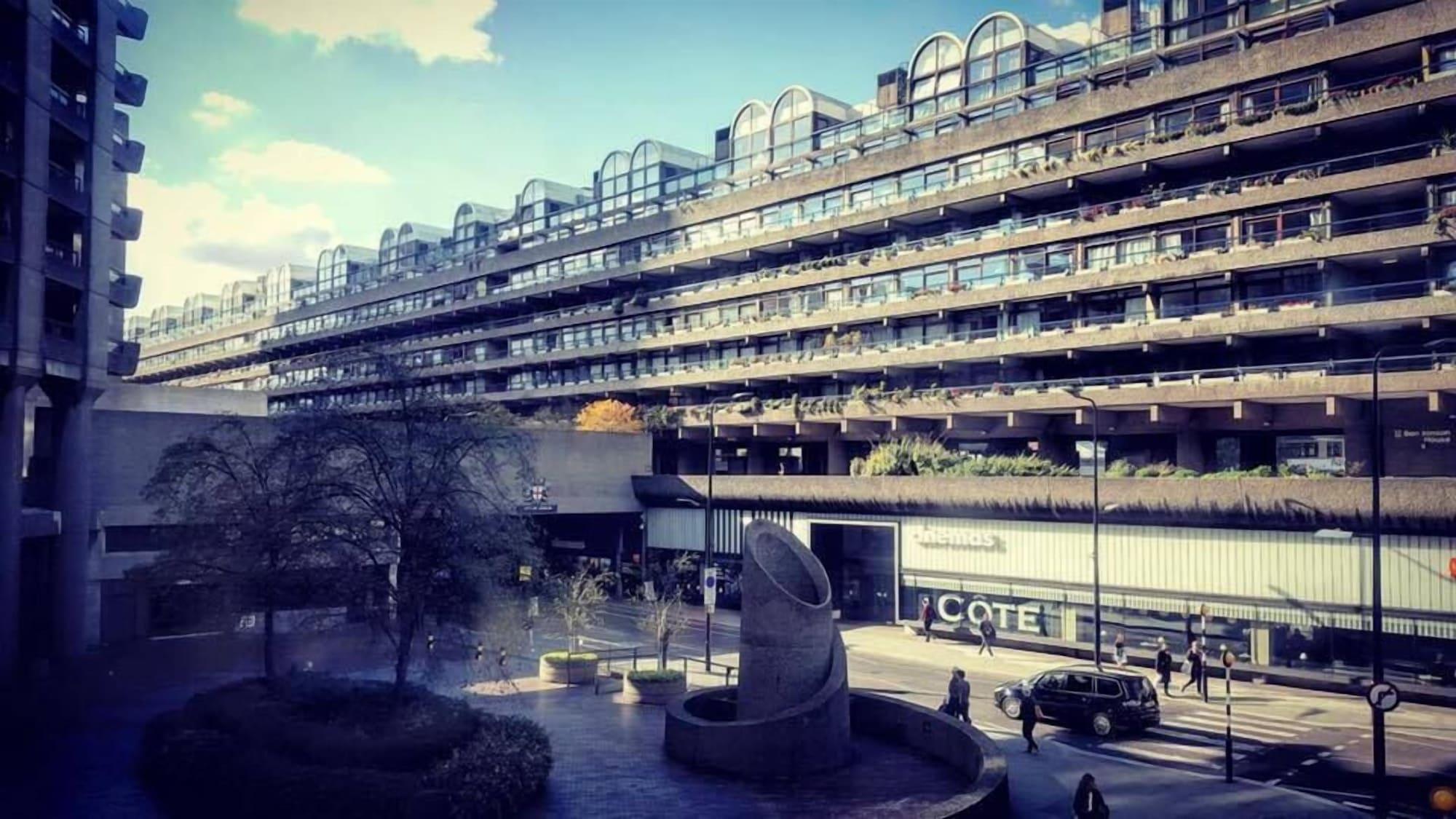 Montcalm Brewery Townhouse Londres Exterior foto The photo shows a modern architectural structure with multiple levels, featuring a series of large, rectangular balconies. Below this building, there is a plaza or courtyard area with a sculptural piece, which appears to be made of stone. Surrounding