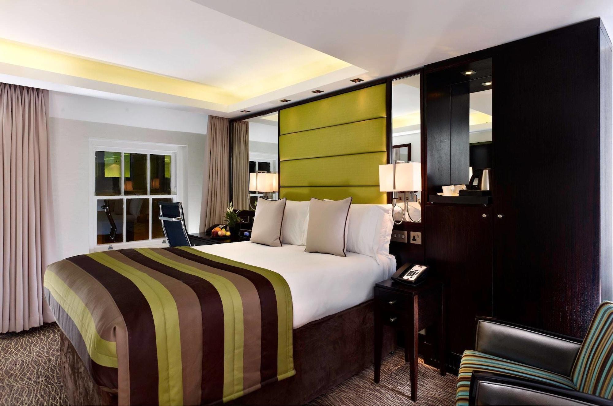 Montcalm Brewery Townhouse Londres Exterior foto The photo shows a modern hotel room featuring a large bed with a striped comforter in shades of green, brown, and cream. The bed is adorned with several decorative pillows. Behind the bed, there is a contemporary headboard with a green panel design. 