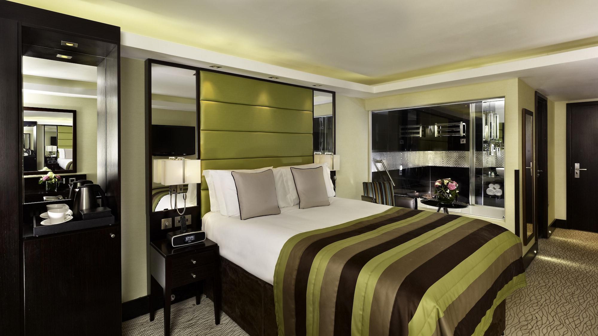 Montcalm Brewery Townhouse Londres Exterior foto The photo shows a modern hotel room designed with a sophisticated aesthetic. It features a comfortable double bed with a striped brown and green bedspread, complemented by two light gray decorative pillows. Behind the bed is an elegant headboard sect