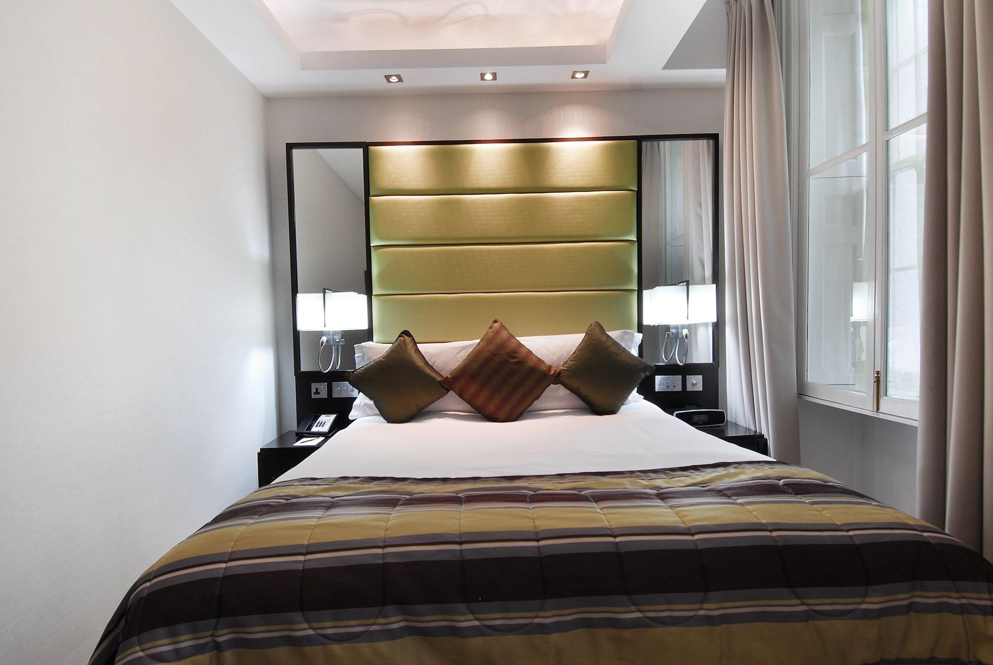 Montcalm Brewery Townhouse Londres Exterior foto The photo shows a stylishly decorated bedroom. The bed is centered in the room, featuring a white comforter with a plaid pattern in shades of brown and green. There are three decorative pillows on the bed, two in shades of brown and one in dark green