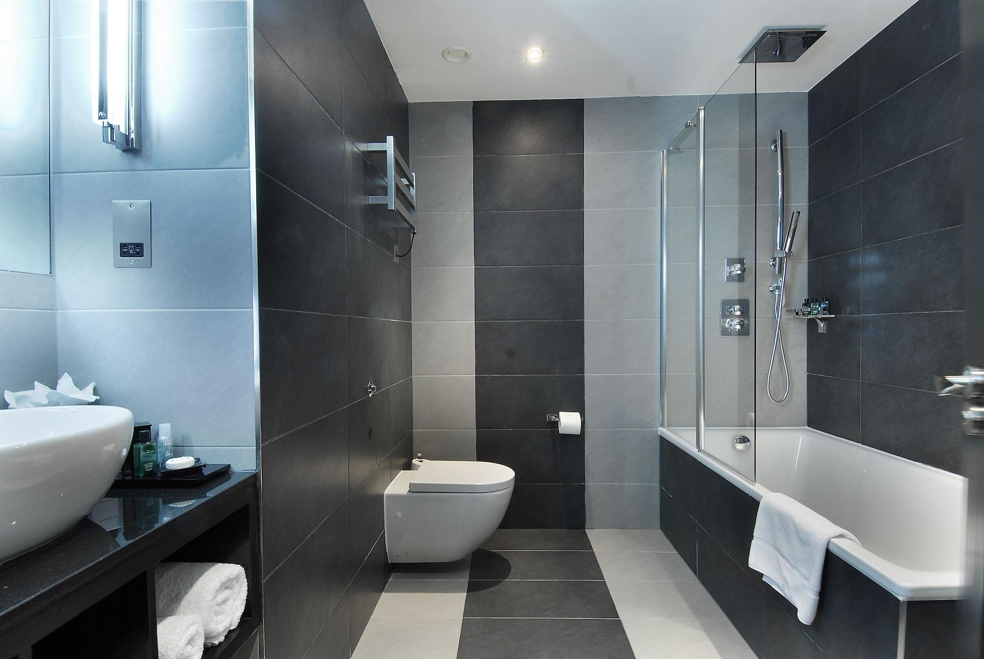 Montcalm Brewery Townhouse Londres Exterior foto The photo shows a modern bathroom featuring a sleek design. The walls are tiled in a combination of dark gray and light gray, creating a contemporary look. On the left, there is a countertop with a basin and some toiletries placed on it. The middle s