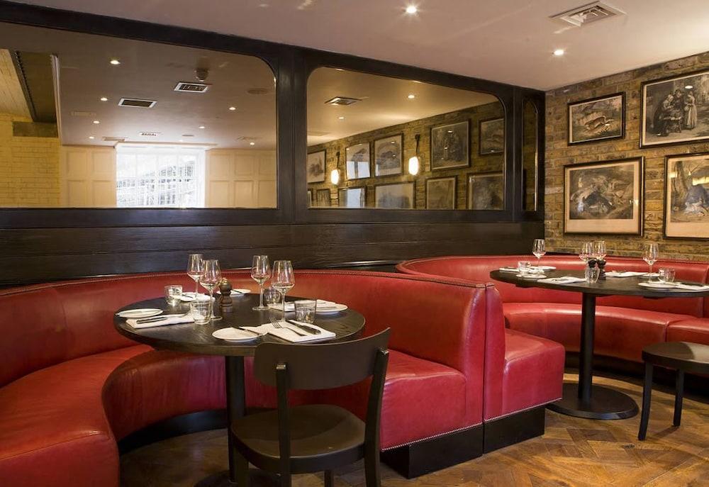 Montcalm Brewery Townhouse Londres Exterior foto The image shows the interior of a restaurant featuring a warm and inviting atmosphere. There are several round tables surrounded by black chairs, with red, upholstered booths lining the walls. The decor includes framed artwork hanging on the walls, a