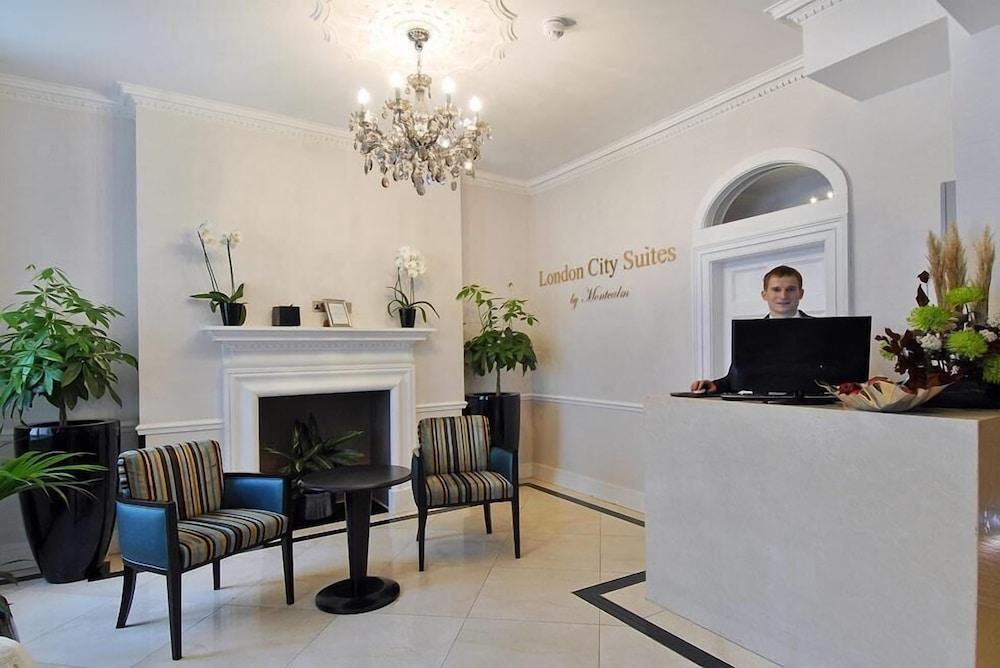 Montcalm Brewery Townhouse Londres Exterior foto The photo shows the interior of a reception area in a hotel called "London City Suites." The space features a light-colored wall with the hotel's name displayed. There is a stylish chandelier hanging from the ceiling, providing warm lighting. 

In th