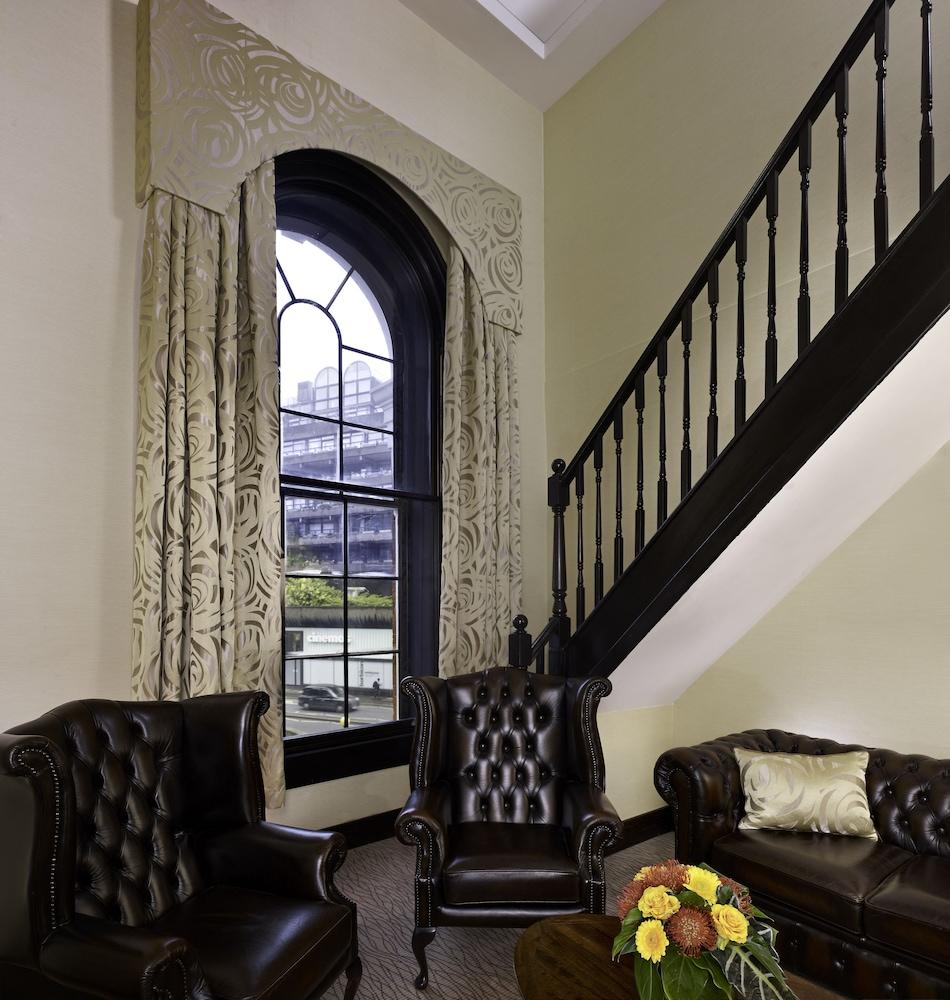 Montcalm Brewery Townhouse Londres Exterior foto The photo shows a cozy interior space featuring two elegant leather armchairs placed near a large, ornate window with arched top and decorative curtains. The wall is painted in a muted color, enhancing the warmth of the room. A staircase with black s