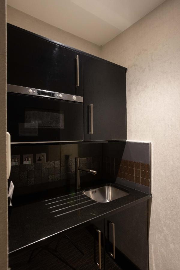 Montcalm Brewery Townhouse Londres Exterior foto The photo shows a modern kitchen setup with a dark color scheme. It features:

- A built-in microwave oven situated above a countertop.
- A sleek black cabinet beneath the microwave, which likely stores kitchen items.
- A stainless steel sink placed 
