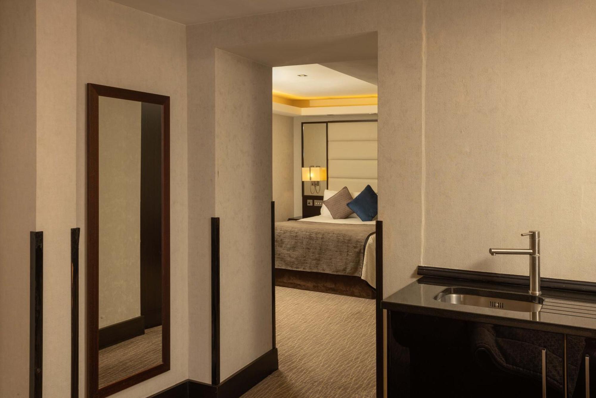 Montcalm Brewery Townhouse Londres Exterior foto The photo shows an interior space that appears to be part of a hotel room or suite. There is a doorway leading into a bedroom area, where a bed with decorative pillows is visible. In the foreground, there's a tall mirror on the left side and a small 