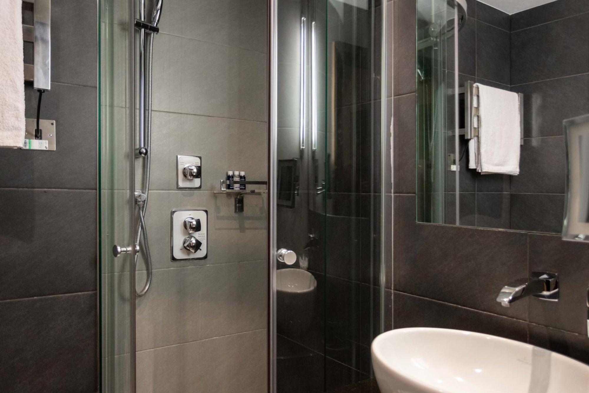 Montcalm Brewery Townhouse Londres Exterior foto The photo shows a modern bathroom with a glass shower enclosure. The shower features a handheld showerhead and various controls mounted on the wall. The walls are tiled in dark, sleek tones, contributing to a contemporary aesthetic. There is a round 