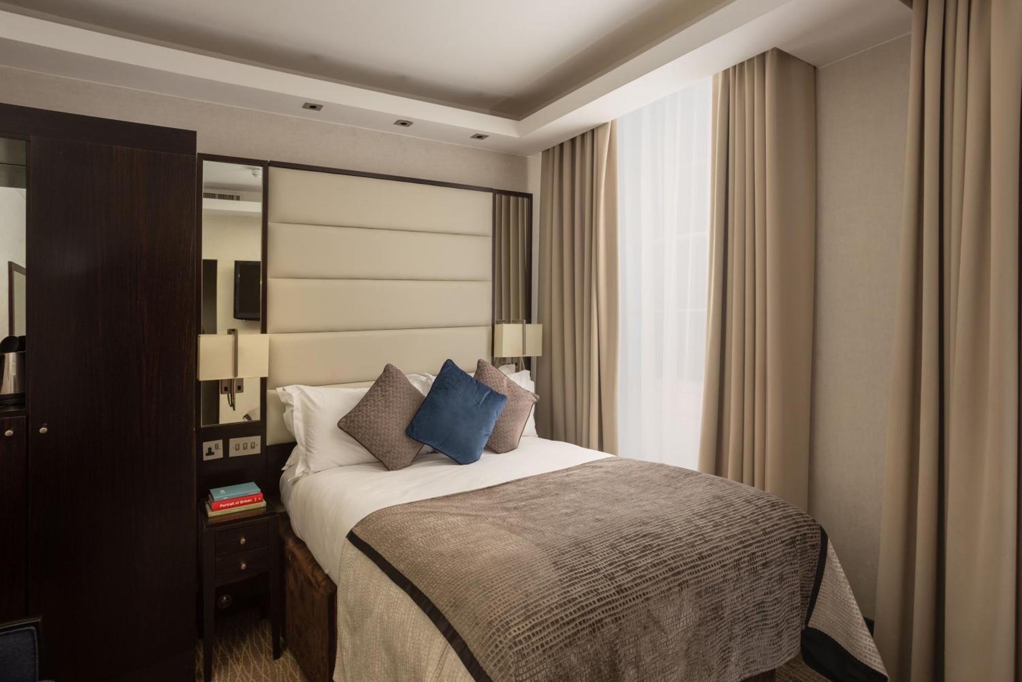 Montcalm Brewery Townhouse Londres Exterior foto The photo shows a modern hotel room with a cozy design. It features a double bed with a light-colored headboard and a soft, stylish blanket. There are decorative pillows on the bed, including a blue one. On either side of the bed, there are small nig