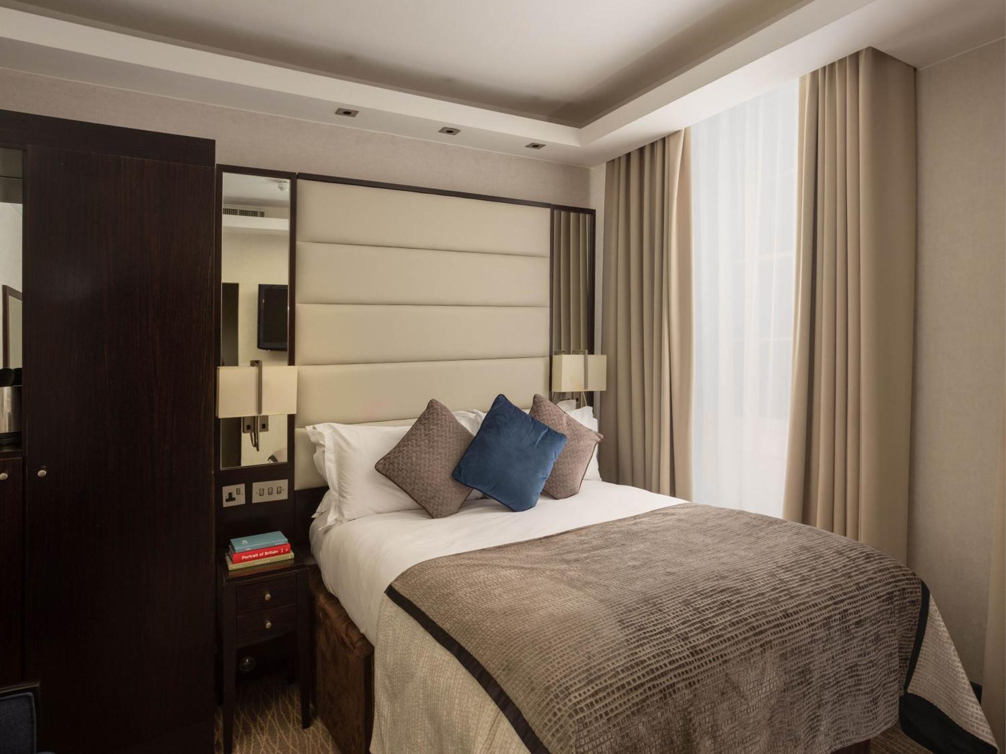 Montcalm Brewery Townhouse Londres Exterior foto The image shows a cozy bedroom. It features a comfortable double bed with a light-colored duvet and decorative pillows in shades of blue and gray. The headboard is upholstered in a soft material, and there are bedside lamps on either side of the bed.