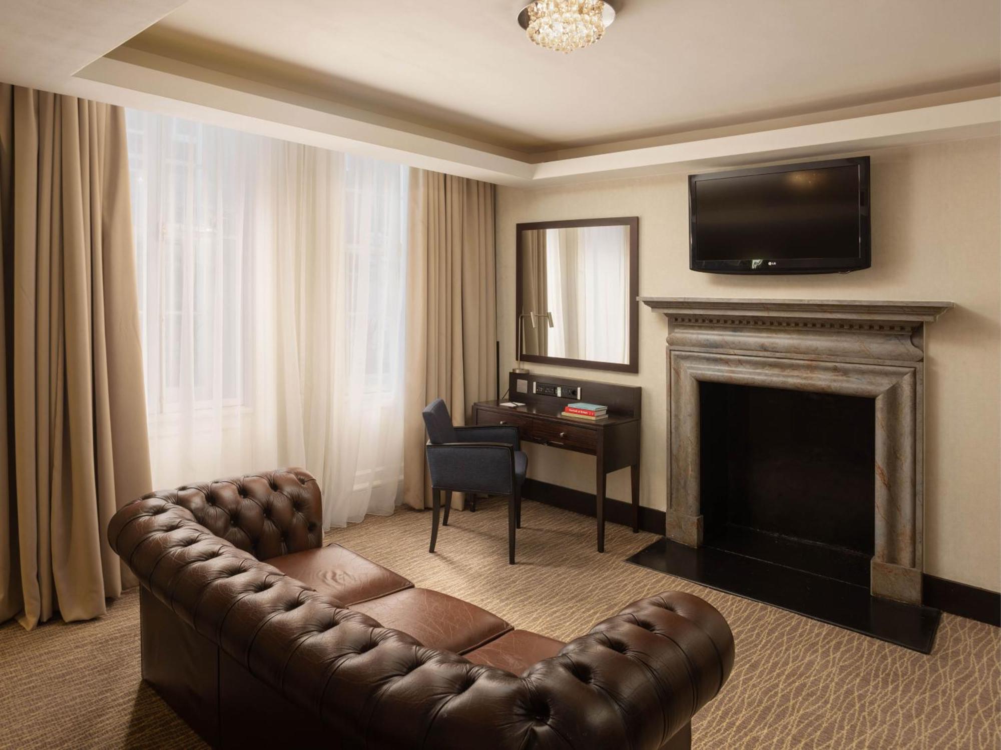 Montcalm Brewery Townhouse Londres Exterior foto The photo shows a cozy and elegantly designed room. There is a comfortable brown leather sofa with tufted detailing. A small desk and chair are positioned near a mirror, providing a space for work or personal grooming. On the wall, a flat-screen TV i