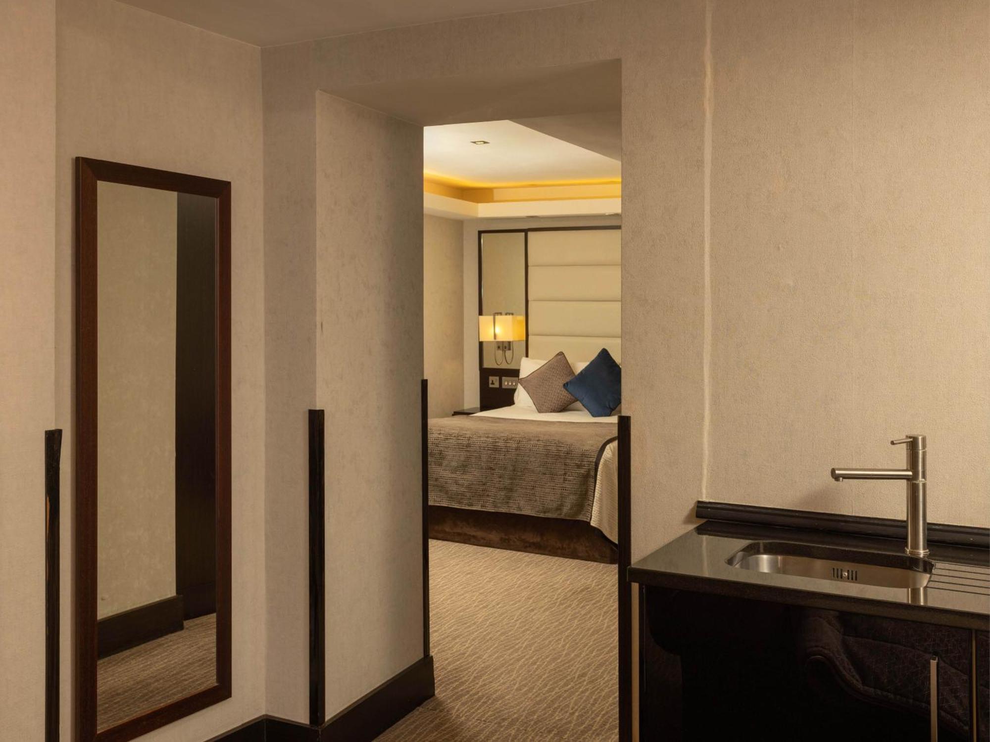 Montcalm Brewery Townhouse Londres Exterior foto The photo shows an interior space that appears to be a hotel room or a suite. There is a doorway leading to a bedroom visible in the background, where a bed with decorative pillows can be seen. To the side, there is a small wet bar or kitchenette are