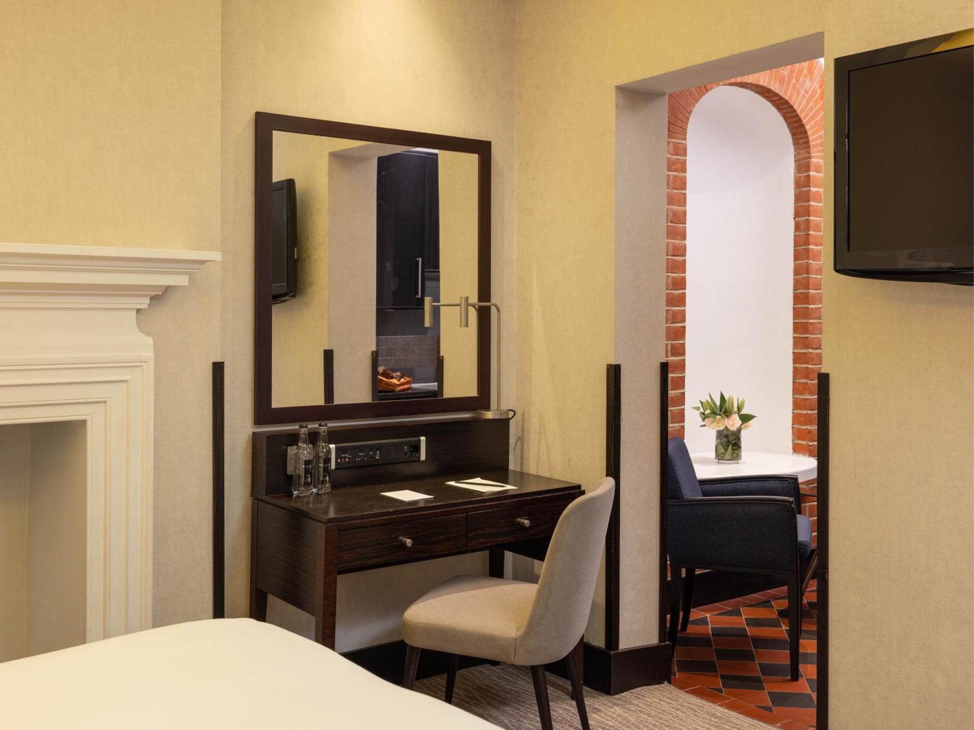 Montcalm Brewery Townhouse Londres Exterior foto The photo displays a hotel room setup. On the left side, there's a bed with a simple white bedding arrangement. Adjacent to the bed, there's a wooden desk with a chair, along with a mirror above the desk. The desk area is equipped with some glassware