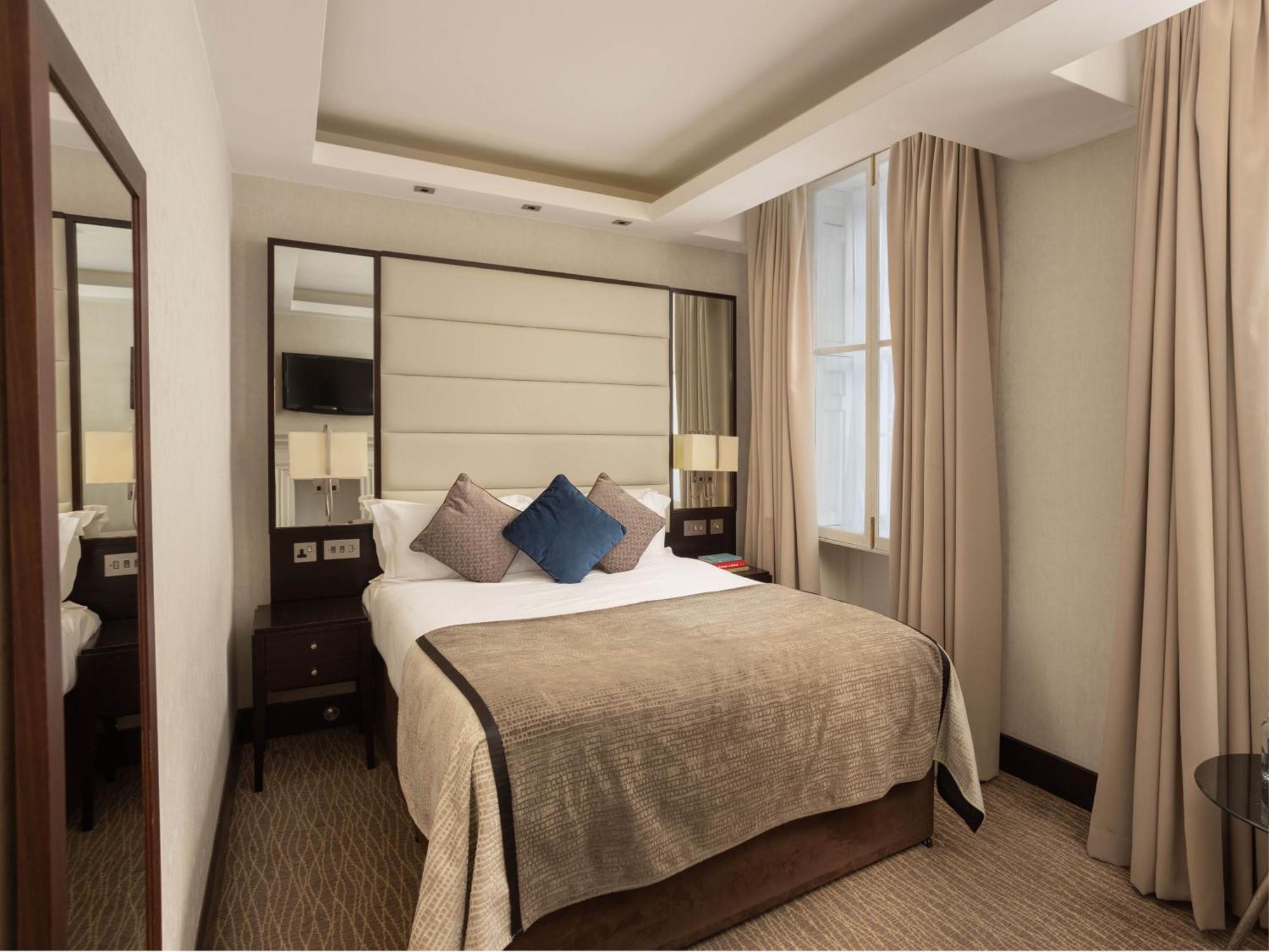 Montcalm Brewery Townhouse Londres Exterior foto The photo shows a cozy hotel room with a bed as the focal point. The bed is made with neutral-colored linens and has several pillows, including a decorative blue one. There are bedside tables on either side of the bed, each with a lamp. A large mirro