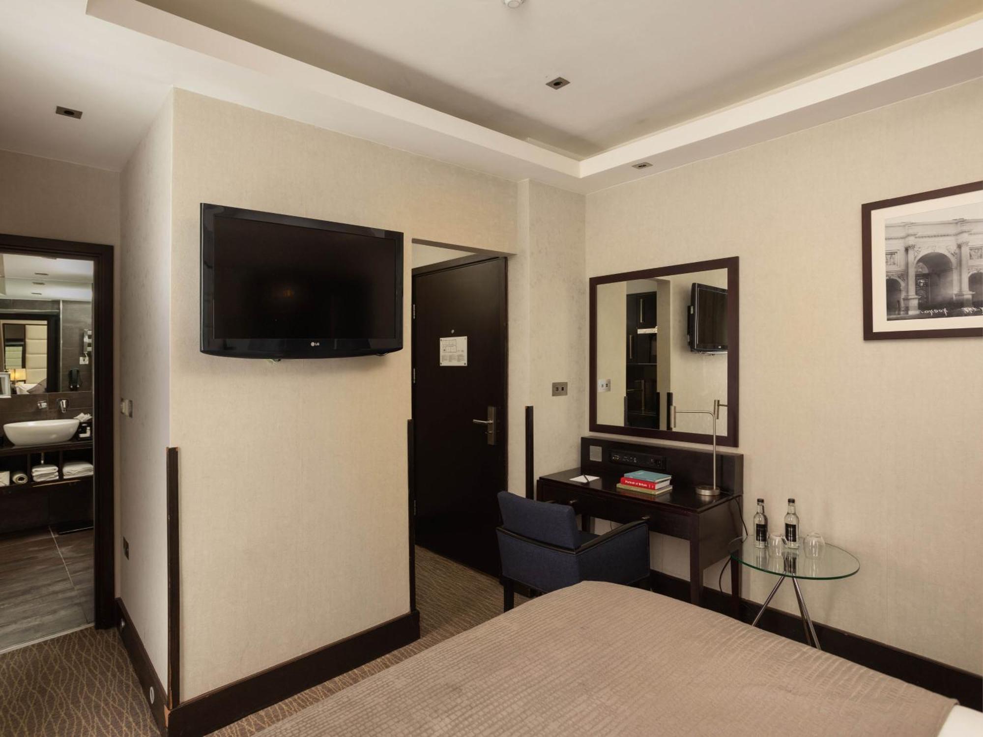 Montcalm Brewery Townhouse Londres Exterior foto The photo shows a hotel room with a modern and minimalist design. On the left, there's a wall-mounted flat-screen TV. In the center, there's a bed with a neutral-colored bedspread. To the right of the bed, there is a small desk with a mirror above it