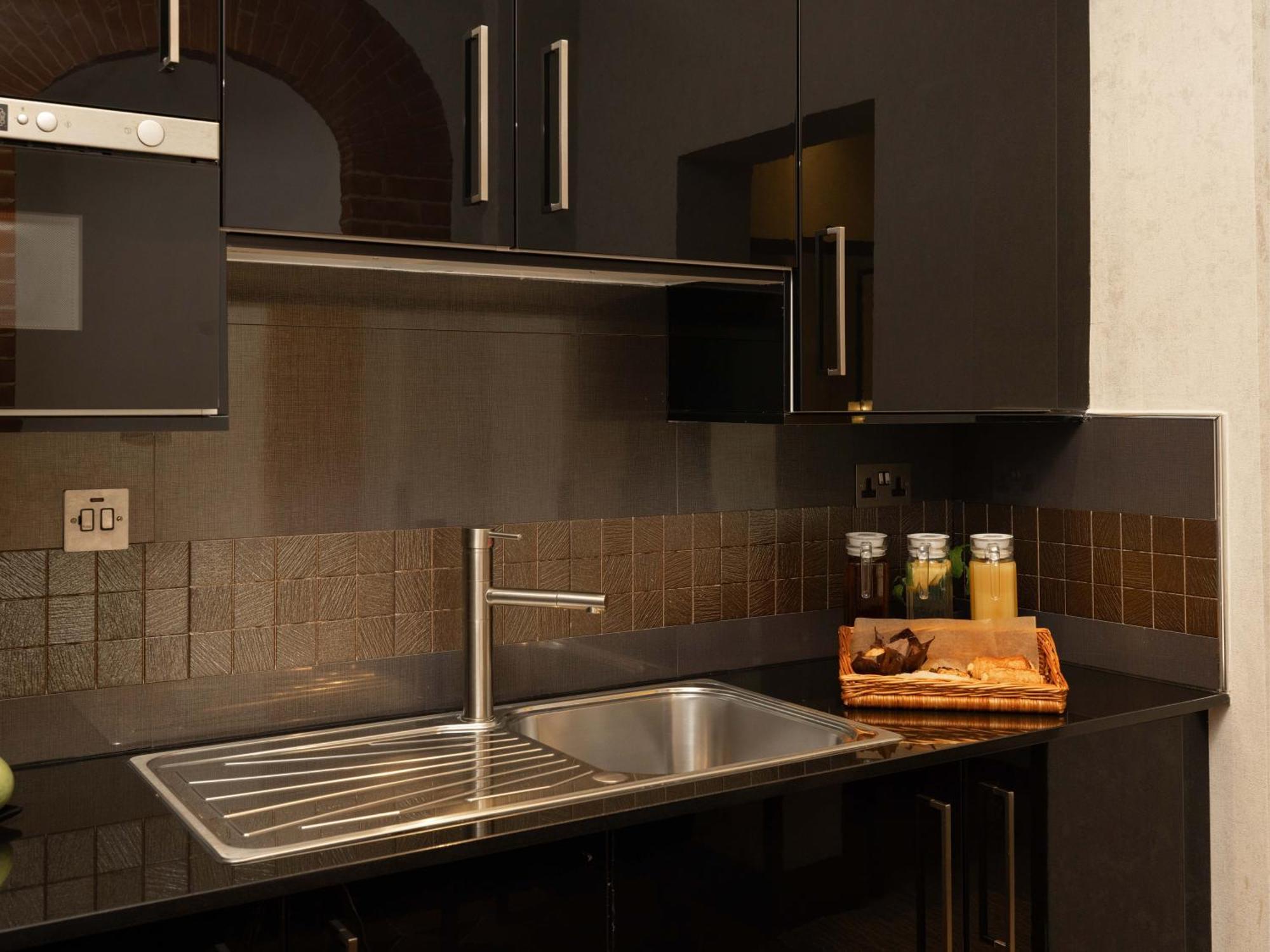 Montcalm Brewery Townhouse Londres Exterior foto The photo shows a modern kitchen with a sleek design. It features dark cabinetry with a glossy finish and stainless steel handles. There is a stainless steel sink with a simple faucet, and a countertop made of black material. Above the sink, there ar
