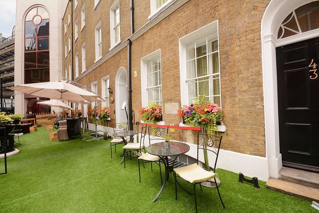 Montcalm Brewery Townhouse Londres Exterior foto The photo depicts a charming outdoor area in front of a building with a warm, textured brick facade. There is a neatly maintained lawn, likely made of artificial grass, and several small round tables with chairs are arranged outside. Flower pots with