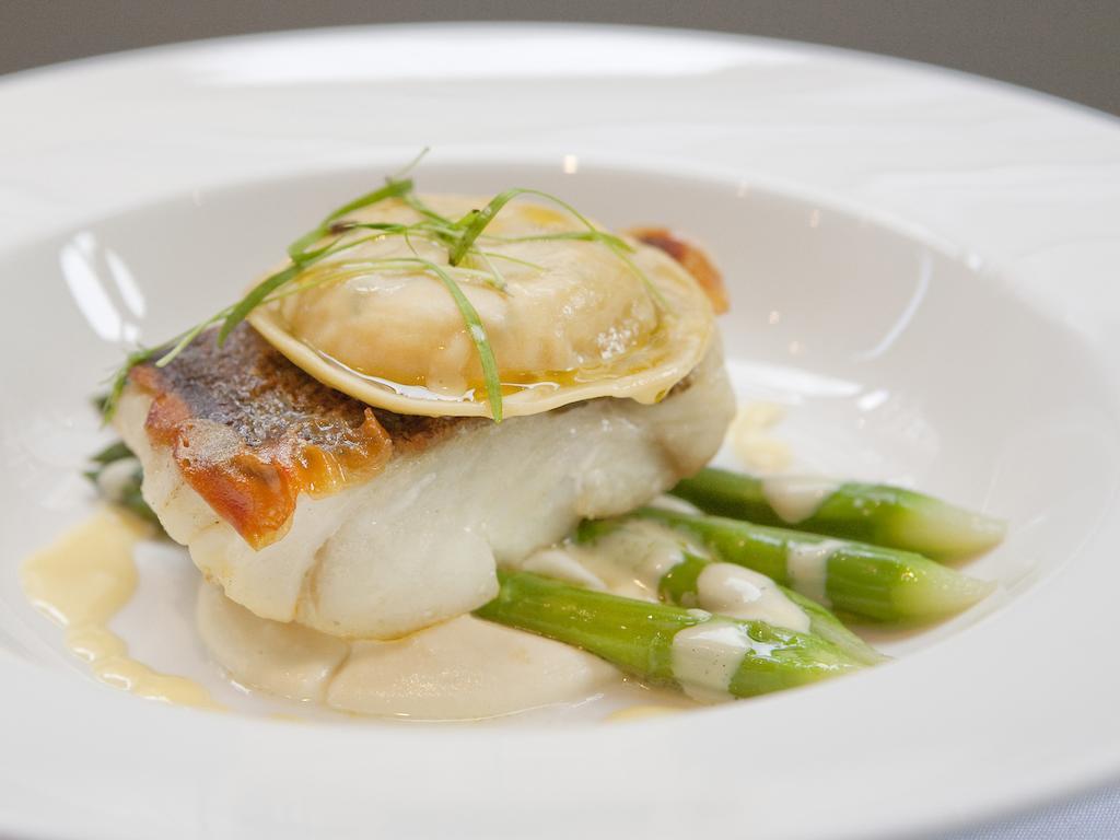 Montcalm Brewery Townhouse Londres Exterior foto The image shows a beautifully presented dish featuring a piece of fish, likely a white fish, topped with a clam. It is served on a bed of green asparagus spears. The dish is garnished with thinly sliced herbs or greens, adding a touch of color. The s