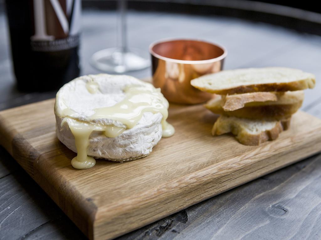 Montcalm Brewery Townhouse Londres Exterior foto The photo features a wooden serving board with several items. There is a round cheese, likely Brie or a similar soft cheese, that appears to be melting and dripping slightly. Next to the cheese, there is a small copper cup that might contain a sauce 