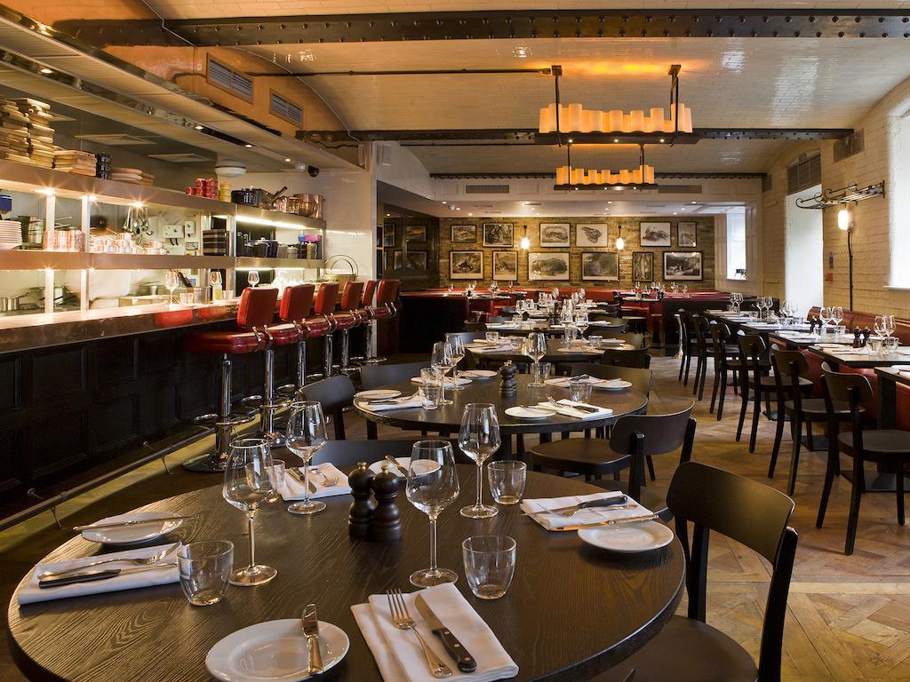 Montcalm Brewery Townhouse Londres Exterior foto The photo shows the interior of a stylish restaurant. It features several round tables set with white plates, glasses, and silverware, all neatly arranged for dining. The decor includes a modern design with wooden floors and a mix of lighting fixture