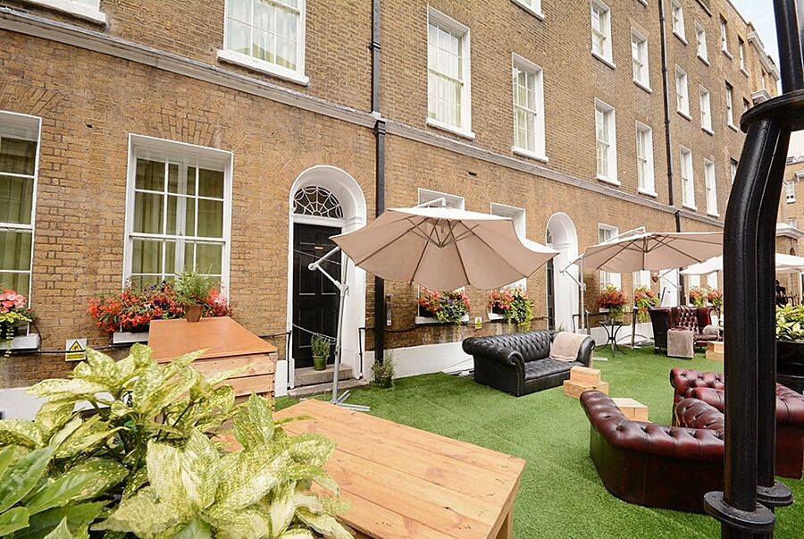 Montcalm Brewery Townhouse Londres Exterior foto The photo depicts an outdoor area of a building with a brick facade. There are several large windows visible, along with a wooden door. The setting features outdoor furniture, including couches in a dark leather finish and wooden tables. Large umbrel